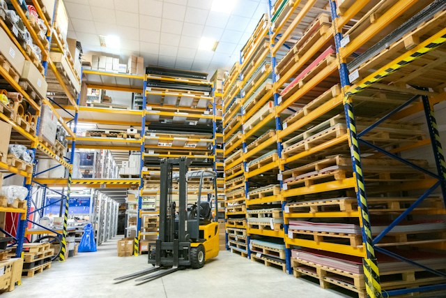 A yellow forklift in a warehouse, surrounded by shelves with boxes on them