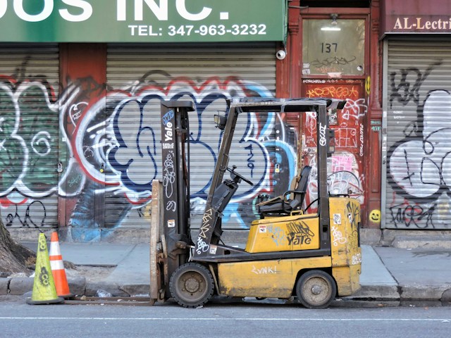 A forklift parked on the side of the street, with graffiti on it